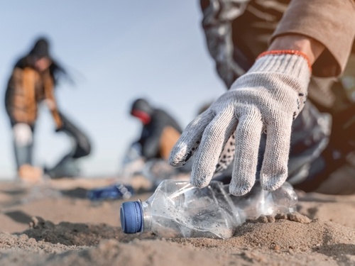 A person is picking up a plastic bottle on the beach