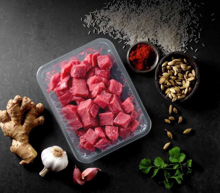 Fresh diced raw beef in a clear plastic food packaging tray with herbs and spices, showcasing durable food-grade plastic packaging solutions.