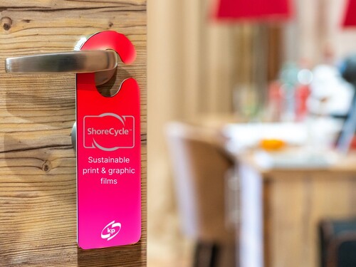 The picture is showing a hanging door sign made out of PCR sustainable Shorecycle plastic film