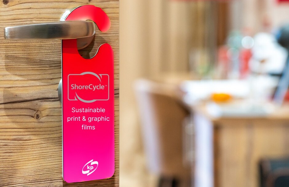 The picture is showing a hanging door sign made out of PCR sustainable Shorecycle plastic film